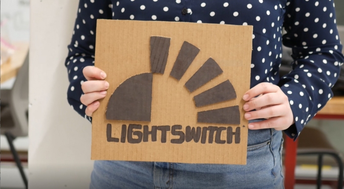 student holds carboard sign saying Lightswitch